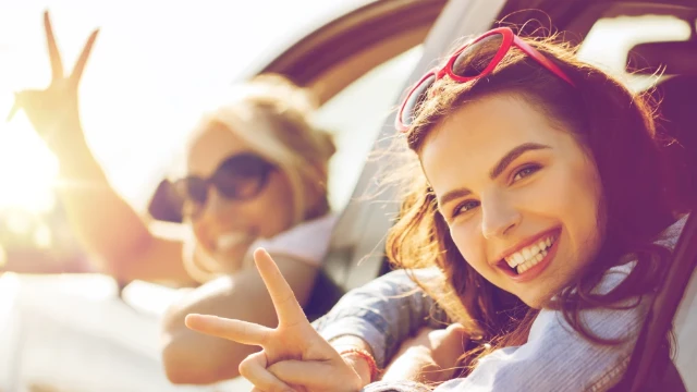 Dos mujeres felices saludando por la ventana de su auto con la tranquilidad de tener un seguro con Donna.