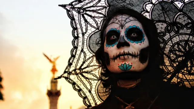 Mujer con maquillaje de catrina y sombrilla frente al Ángel de la Independencia en CDMX, representando el orgullo mexicano en el contexto de inversión local.