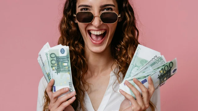 Mujer con gafas sosteniendo billetes de 100 euros sobre fondo rosado