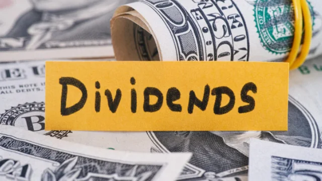 Billetes junto a un letrero amarillo con la palabra “dividends”, representando ingresos pasivos por inversiones.