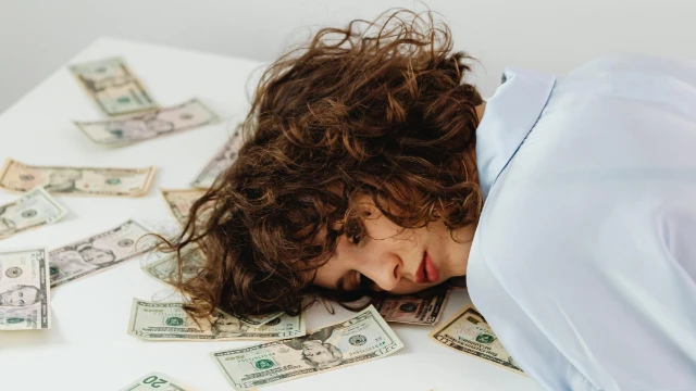 Mujer con la cabeza recostada sobre la mesa, rodeada de billetes, con expresión de frustración por la inflación