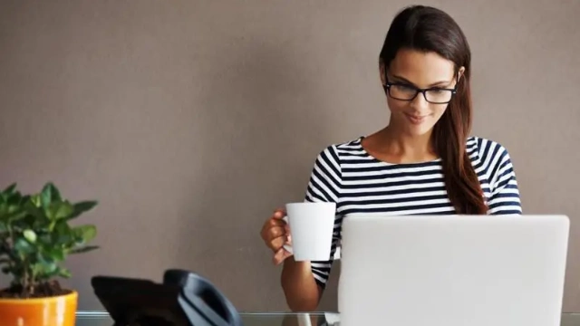 Mujer feliz frente a su MacBook con un café, representando tranquilidad financiera al invertir para el retiro
