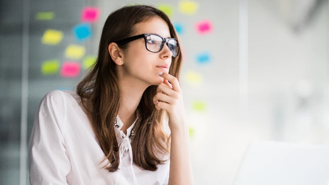 Mujer pensativa con la mano en la cara, frente a una pared blanca, simbolizando dudas sobre contratar un seguro médico en México.