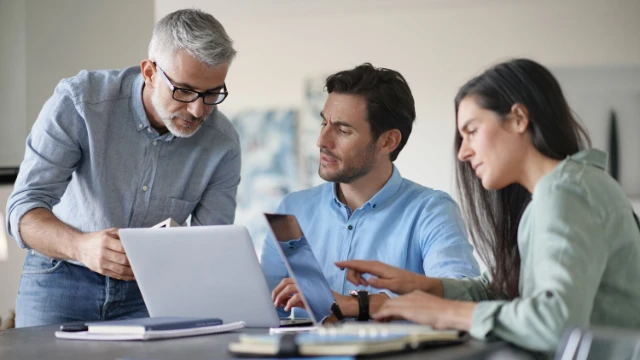 Tres personas revisando documentos y laptop mientras analizan opciones de inversión para RESICO.