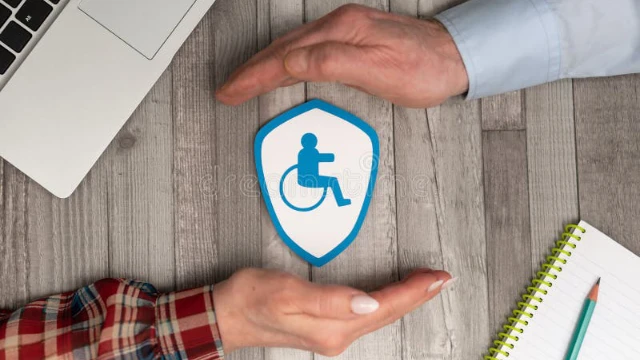 Manos cubriendo protectoramente una figura de papel de una persona en silla de ruedas representando protección financiera y seguro por invalidez